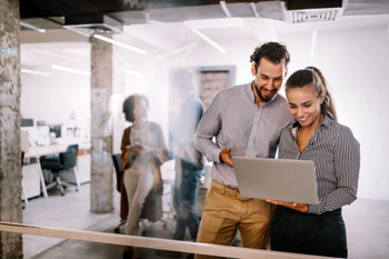 Un hombre y una mujer de pie revisando información en un computador portátil
